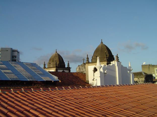 Stadtansicht mit Gebäuden im Vordergrund und einem blauen Himmel im Hintergrund, die Solarpanels auf einem Dach zeigen.