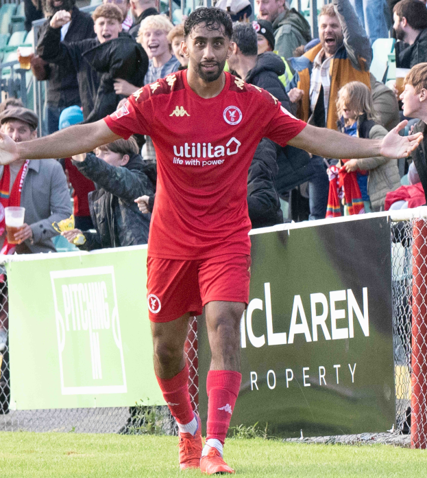 Ein Fußballspieler in roter Uniform rennt mit ausgestreckten Armen auf einem Feld, mit einer Menge im Hintergrund und einem Banner mit der Aufschrift "Middlesbrough FC v Swansea City - Sky Bet Championship" im Vordergrund.