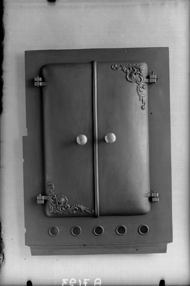 Ein Schwarz-Weiß-Foto eines Metallschranks mit einer leicht geöffneten rechteckigen Tür, die einen gebogenen silbernen Griff auf der Oberseite aufweist.