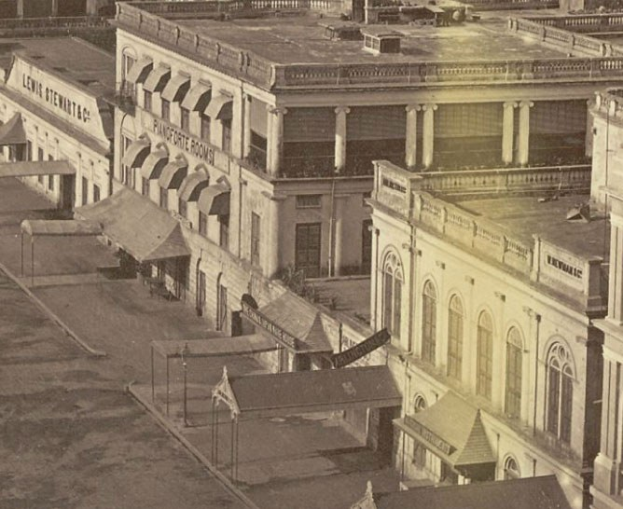 Altes Schwarz-Weiß-Foto einer Straße mit Gebäuden, Fenstern, Säulen, Namensschildern, Hütten und Masten.