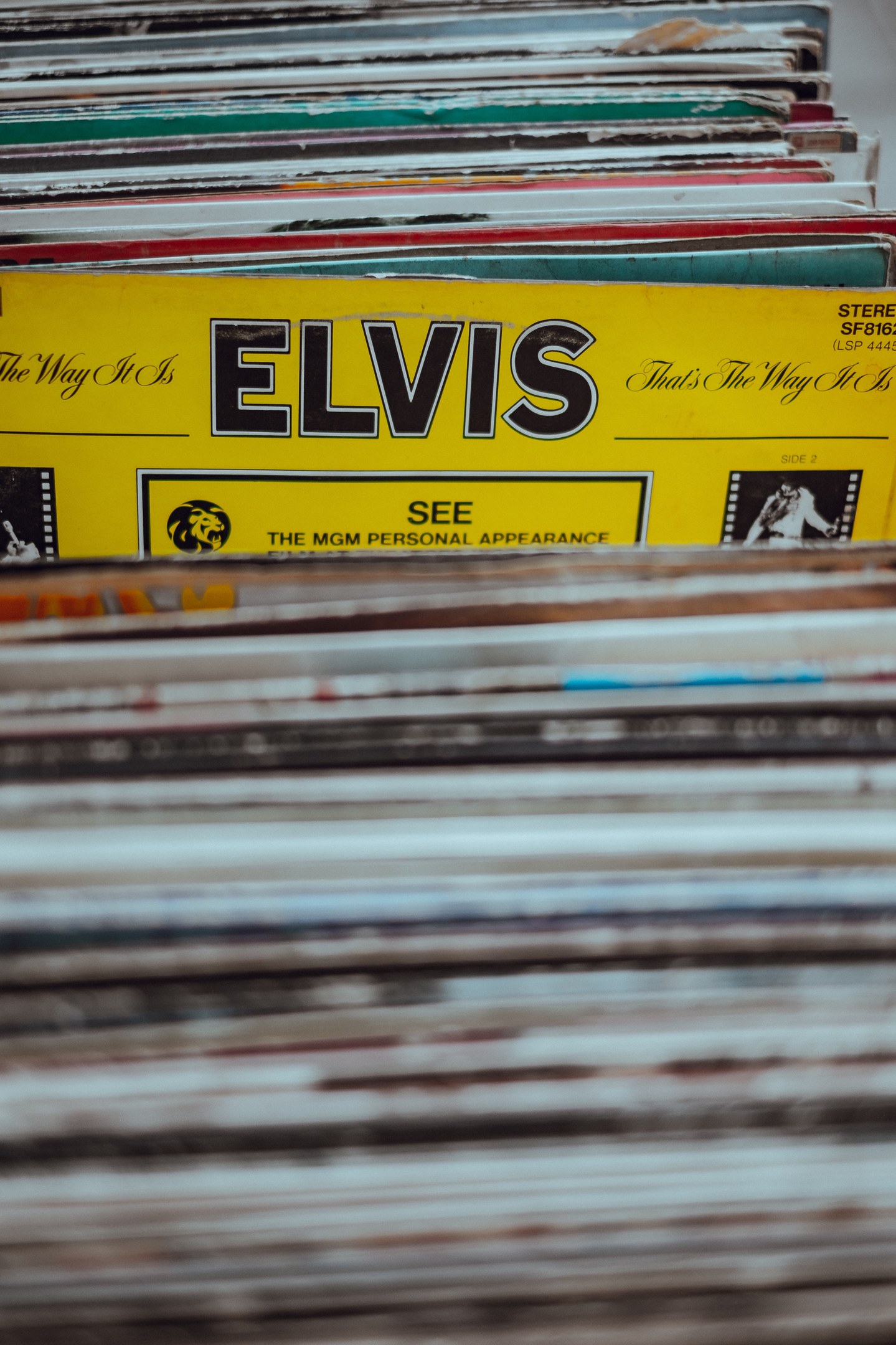 Stapel von Elvis-Presley-Platten in einem ordentlichen, überlappenden Stapel auf einem Tisch mit sichtbaren Titeln und einem leicht unscharfen, träumerischen Hintergrund.