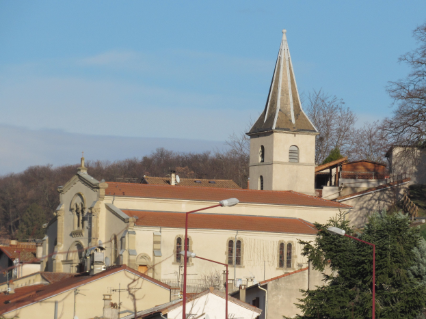 Eine Stadtansicht mit einer zentralen Kirche umgeben von Gebäuden, Laternenmasten, Straßenlaternen, Bäumen und einem bewölkten Himmel.