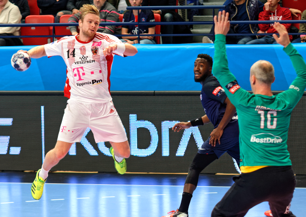 Eine Gruppe von Männern, die auf einem Handballfeld mit einem Ball in der Mitte spielen, während Zuschauer von Stühlen und Geländern im Hintergrund zuschauen, mit einer Tafel, auf der "Futsal-Weltmeisterschaft 2019 - Bayern München vs. Paris Saint-Germain" steht.