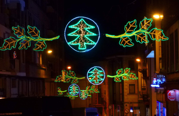 Eine stadtstraße, geschmückt mit festlichen Weihnachtslichtern in Form von Blättern, mit Fahrzeugen und Gebäuden auf beiden Seiten.
