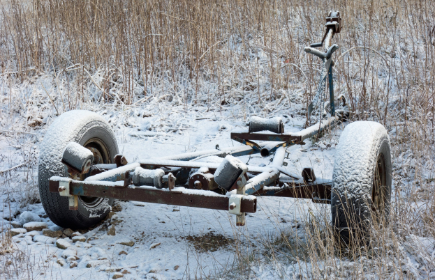 Alter rostiger Anhänger voller Schnee in einem verschneiten Feld mit Gras und Steinen.