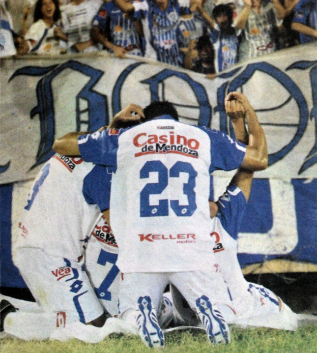 Gruppe von Fußballspielern feiert auf dem Rasen mit einem Banner im Hintergrund, während die Menge jubelt.