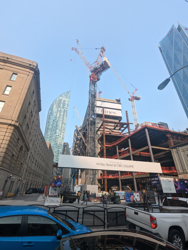 Eine belebte Stadtstraße mit Fahrzeugen, Fußgängern, hohen Gebäuden und einer Baustelle mit einem großen Kran an der 141 Bay Street.