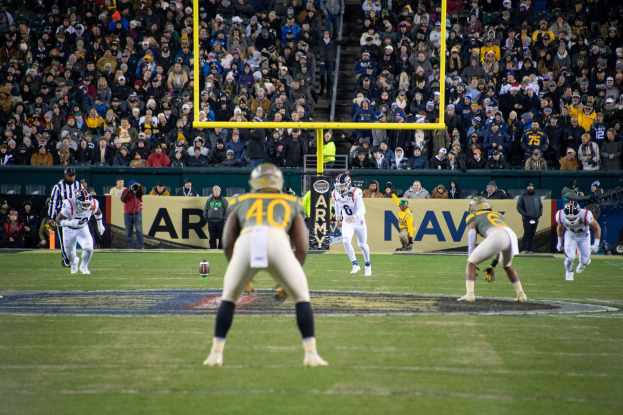 Fußballspieler mit Helmen und Uniformen konkurrieren auf einem Feld mit Zuschauern auf den Rängen und Stadionwerbung.