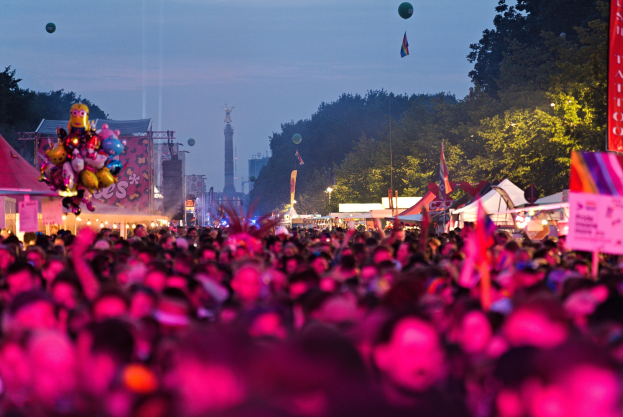 Eine gro├če Menge auf einem nächtlichen Musikfestival mit bunten Lichtern, Ballons, Zelten, Bannern, Fahnen, B├Ąumen und einem Sternenhimmel im Hintergrund.