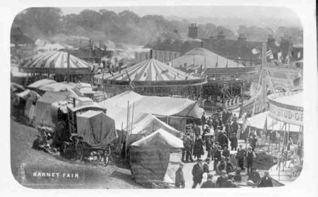 Ein altes Schwarz-Weiß-Foto einer belebten KarnevalsSzene mit Zelten, Menschen, Karren, Pfählen, Bäumen und Gebäuden im Hintergrund, mit dem Text "Barnet Fair, London, England" unten.