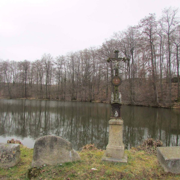 Ein Friedhof mit einem Kreuz in der Mitte eines Sees, umgeben von Bäumen, Gras und verstreuten Grabsteinen unter einem sichtbaren Himmel.