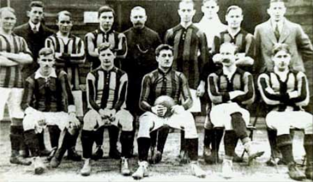 Ein Schwarz-Weiß-Foto einer Fußballmannschaft, einige stehen und einige sitzen vor einer Wand, mit dem Text "Ballymena Football Club" unten.