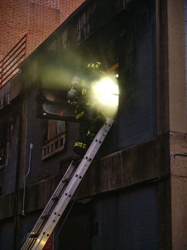 Feuerwehrmann auf einer Leiter vor einem Gebäude, mit Helm und Feuerlöscher, mit Fenstern und Geländer.