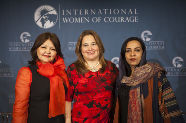 Drei Frauen stehen zusammen vor einem Banner mit der Aufschrift "International Women of Courage".