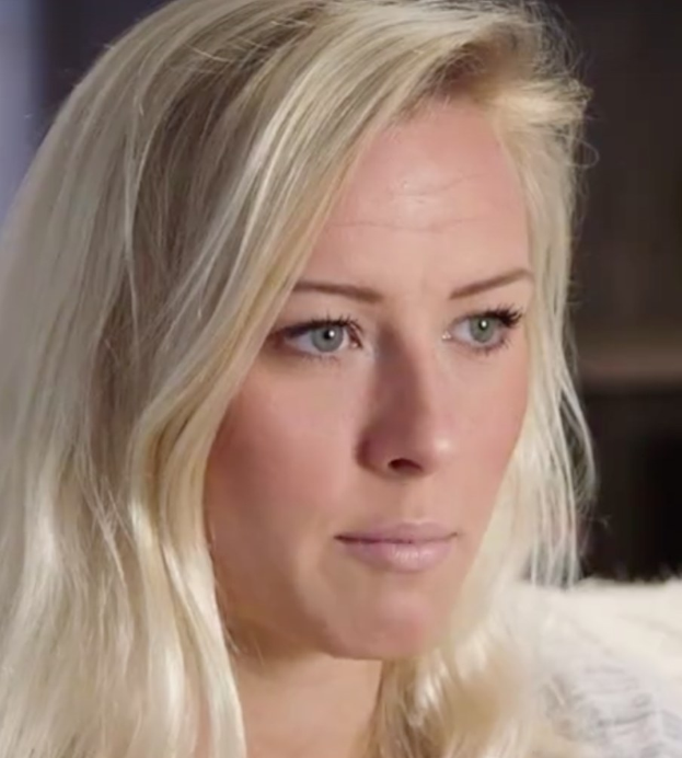 Blonde Frau mit blauen Augen im Vordergrund, die besorgt wirkt, mit einem unscharfen Hintergrund.