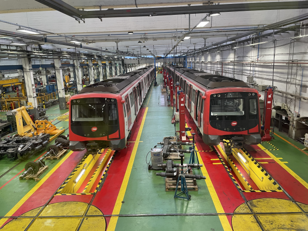 Zwei Züge auf den Schienen in einer Daimler Group-Fabrik mit umgebender Maschine, Rohren und Deckenbeleuchtung.