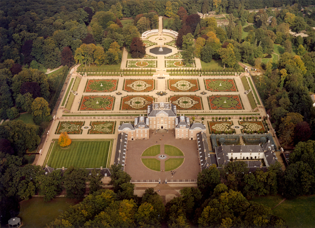 Ein großes Herrenhaus mit einem prächtigen Eingang und mehreren Fenstern, das in der Mitte eines üppigen, grünen Parks mit Bäumen, Pflanzen, Gras und einem Brunnen liegt.