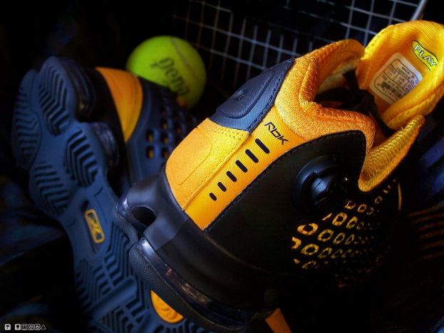 Ein Schuhpaar und ein Ball sind in der Mitte des Bildes zu sehen, im Hintergrund ein Zaun.