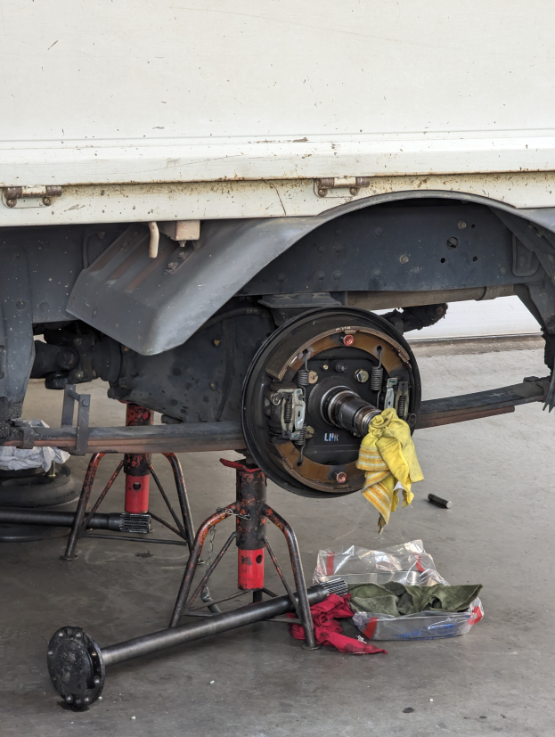 Ein Lastwagen in einer Garage geparkt, mit einem gelben Tuch darüber drapiert, umgeben von verstreuten Werkzeugen und Gegenständen auf dem Boden.