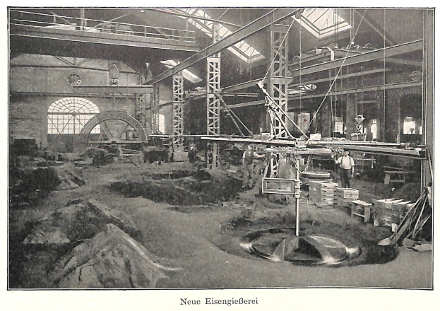 Altes Schwarz-Weiß-Foto einer Fabrikhalle mit Arbeitern an einer Maschine, umgeben von Metallstangen und -rohren, beschriftet mit "Neue Eisengießerei, die erste Fabrik Deutschlands" unten.