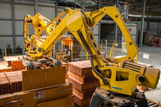 Ein großer Lagerhalle voller numerous boxes, Kräne und verschiedene industrielle Ausrüstung, mit einem Zaun und Pfählen im Vordergrund und einer Wand im Hintergrund.