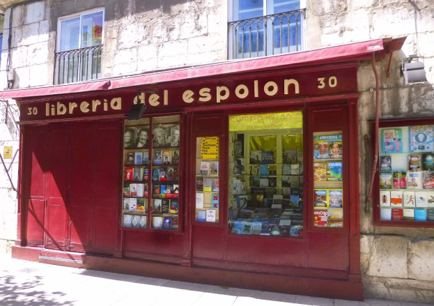 Ein Buchladen namens 'Libreria del Espolon' mit einer roten Markise, der ein Gebäude mit Fenstern, Geländern und ordentlich angeordneten Büchern zeigt.