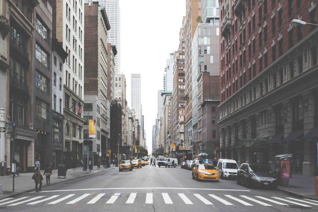 Eine belebte Stadtstraße mit starkem Verkehr, Fußgängern, hohen Gebäuden und Werbetafeln für die Top 10 Dinge, die man in New York City sehen sollte.