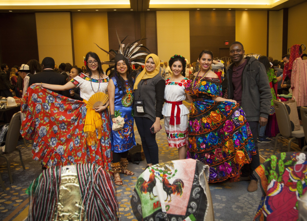 Eine Gruppe von Menschen in bunten Kleidern, die fröhlich posieren und für ein Foto posieren, mit Stühlen, Tischen und Kleidung im Hintergrund.