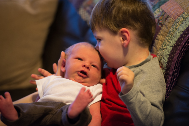 Ein Kind, das ein Baby hält, beide tragen Kleidung in verschiedenen Farben, mit einem unscharfen Hintergrund.