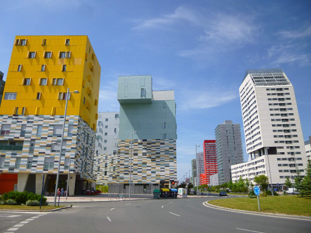 Eine Stadtstraße mit hohen Gebäuden im Hintergrund, Straßenlaternen, Autos, Informationsschildern, Büschen, Bäumen und einer bewölkten Himmel, mit der einzigartigen Architektur der Universität Rotterdam.