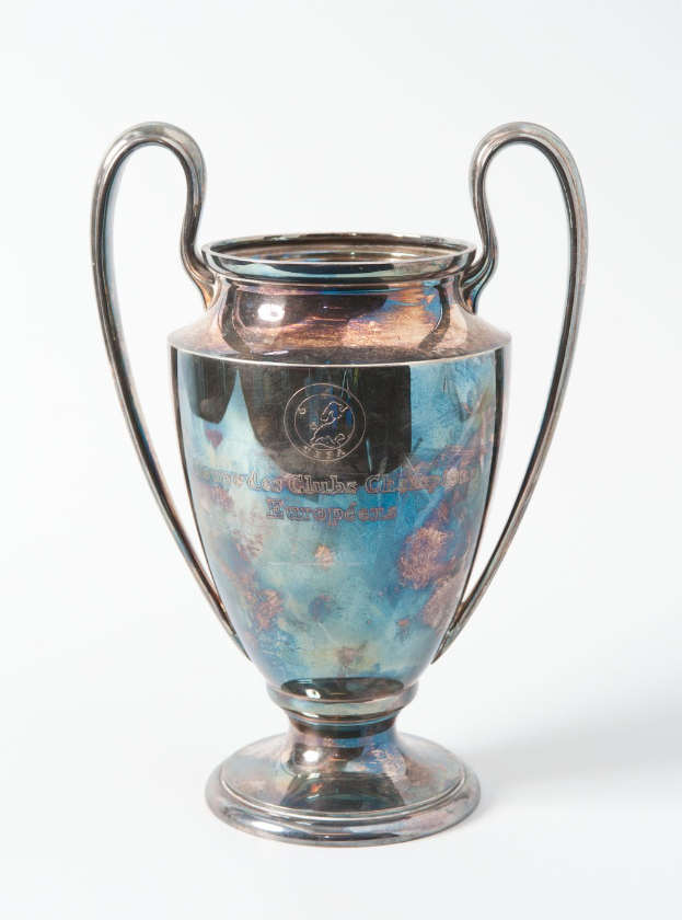 Der UEFA-Champions-League-Pokal, ein stählerner Pokal mit zwei Griffen und einem blauen und silbernen Farbschema, mit der Inschrift "UEFA Champions League", vor einem weißen Hintergrund dargestellt.