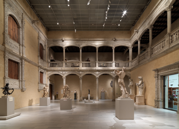 Ein geräumiger Museumsgalerie mit zahlreichen Statuen und Skulpturen auf Sockeln, mit architektonischen Elementen wie Wänden, Säulen, Geländern und Deckenleuchten sowie einigen Besuchern.