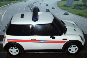 Ein weißes Polizeifahrzeug steht im Vordergrund mit mehreren fahrenden Fahrzeugen auf der Straße dahinter.