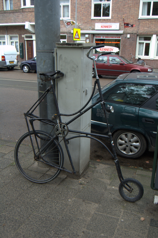 Ein Fahrrad ist in der Nähe von Pfählen, Namensschildern, Fahrzeugen, Gebäuden mit Fenstern und Gardinen sowie Fahnen geparkt.