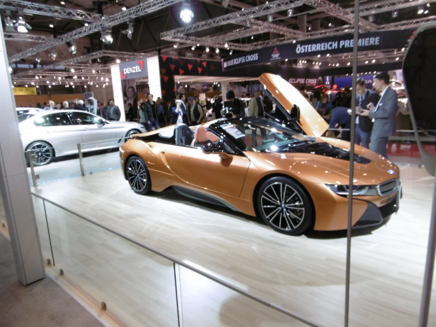Ein schicker schwarzer BMW i8 Roadster mit Chromakzenten auf der Frankfurt Motor Show umgeben von formell gekleideten G├Ąsten.