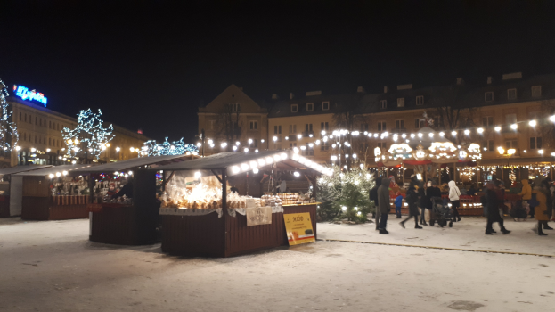Ein festliches Weihnachtsmarkt-Szenario bei Nacht mit Menschen, beleuchteten Buden und schneebedeckter Umgebung.
