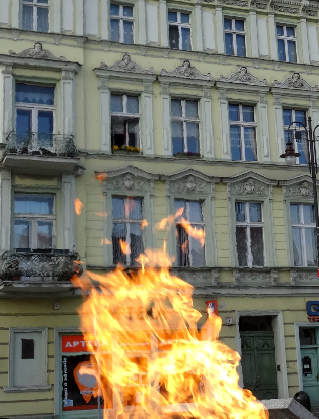 Großer Brand vor einem Gebäude mit Fenstern, Türen, einem Lichtmast und einer Tafel mit Text.